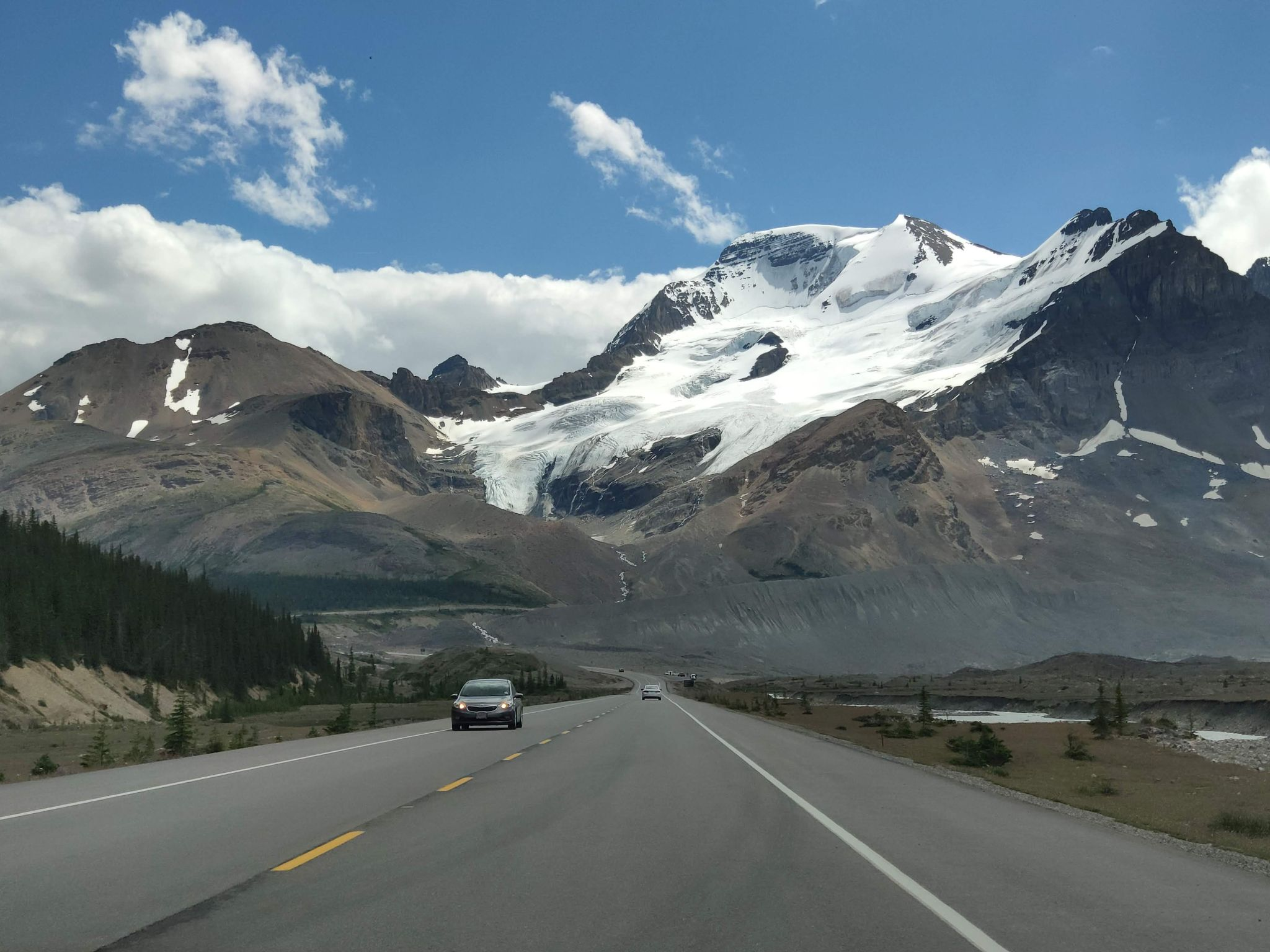 A scenic mountain view from a road trip with a car driving towards the mountains.