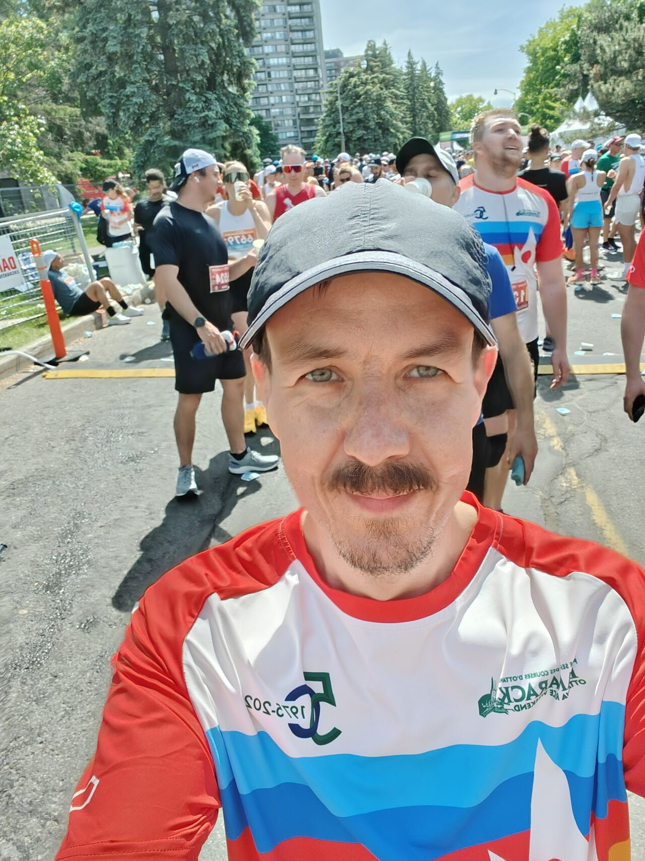 Ildar Akhmetov at the finish line of Ottawa half marathon wearing a colorful running shirt with other runners in the background.